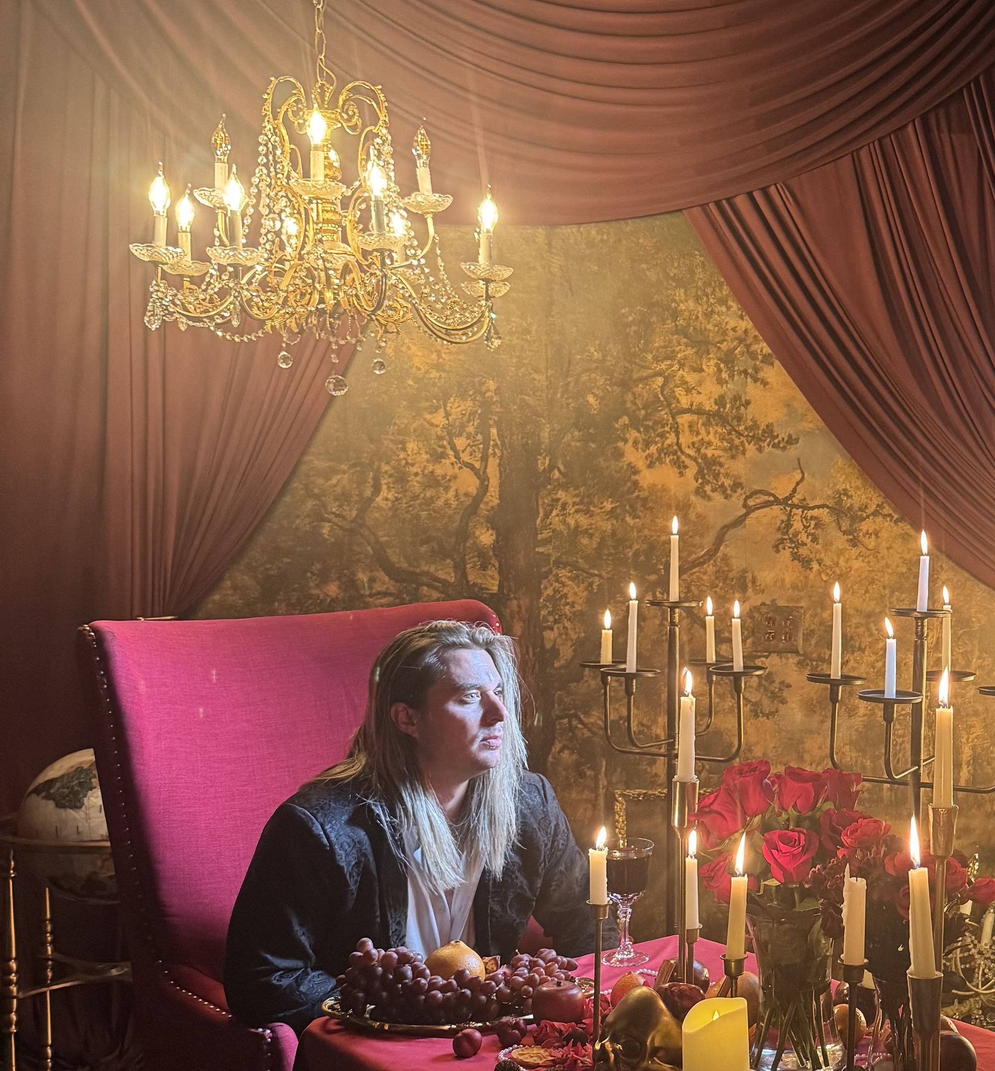 Jay Putty seated at a candlelit banquet table in a red velvet room beneath a chandelier